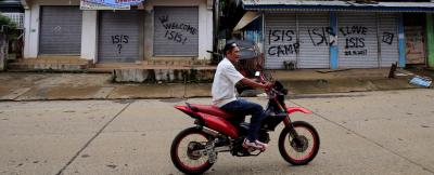 A resident drives past a building with graffiti in Marawi City, Philippines. Credit: Reuters