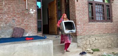 Shafiya Jan* outside her house with broken electronic gadgets. Photo: StandWithKashmir