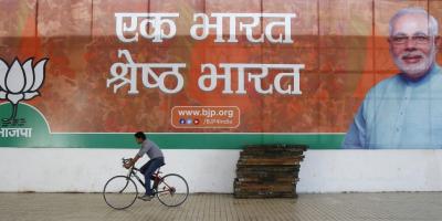 A worker of Bharatiya Janata Party (BJP) rides his bicycle past the party's campaign billboard featuring Prime Minister Narendra Modi outside their party headquarters in New Delhi February 10, 2015. Credit: REUTERS/Anindito Mukherjee/Files