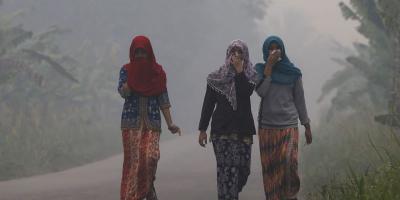 Villagers walk on a street as the haze shrouds Pulau Mentaro village in Muaro Jambi, on the Indonesian island of Sumatra, September 15, 2015.REUTERS/Beawiharta