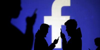 Silhouettes of mobile users are seen next to a screen projection of Facebook logo in this picture illustration taken March 28, 2018. Credit: REUTERS/Dado Ruvic/Illustration/File Photo