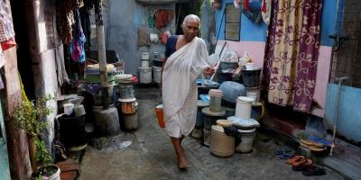 Gita Sen, 70, a widow of a daily wager, who gets an allowance of 1000 rupees from the state government, carries a container with drinking water from a municipal tap outside her rented one-room, in a slum in Kolkata, India, May 23, 2022. REUTERS/Rupak De Chowdhuri