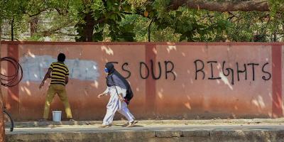 A hijab-wearing student walks past a worker painting a wall to conceal a pro-hijab slogan written on the wall, outside a college, in Hospet, March 16, 2022. Photo: PTI